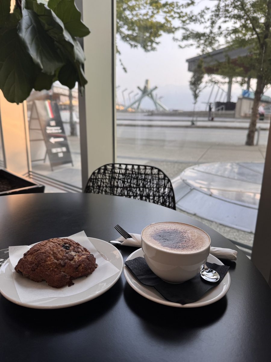 A pastry and a cappuccino on a table by a window overlooking a waterfront