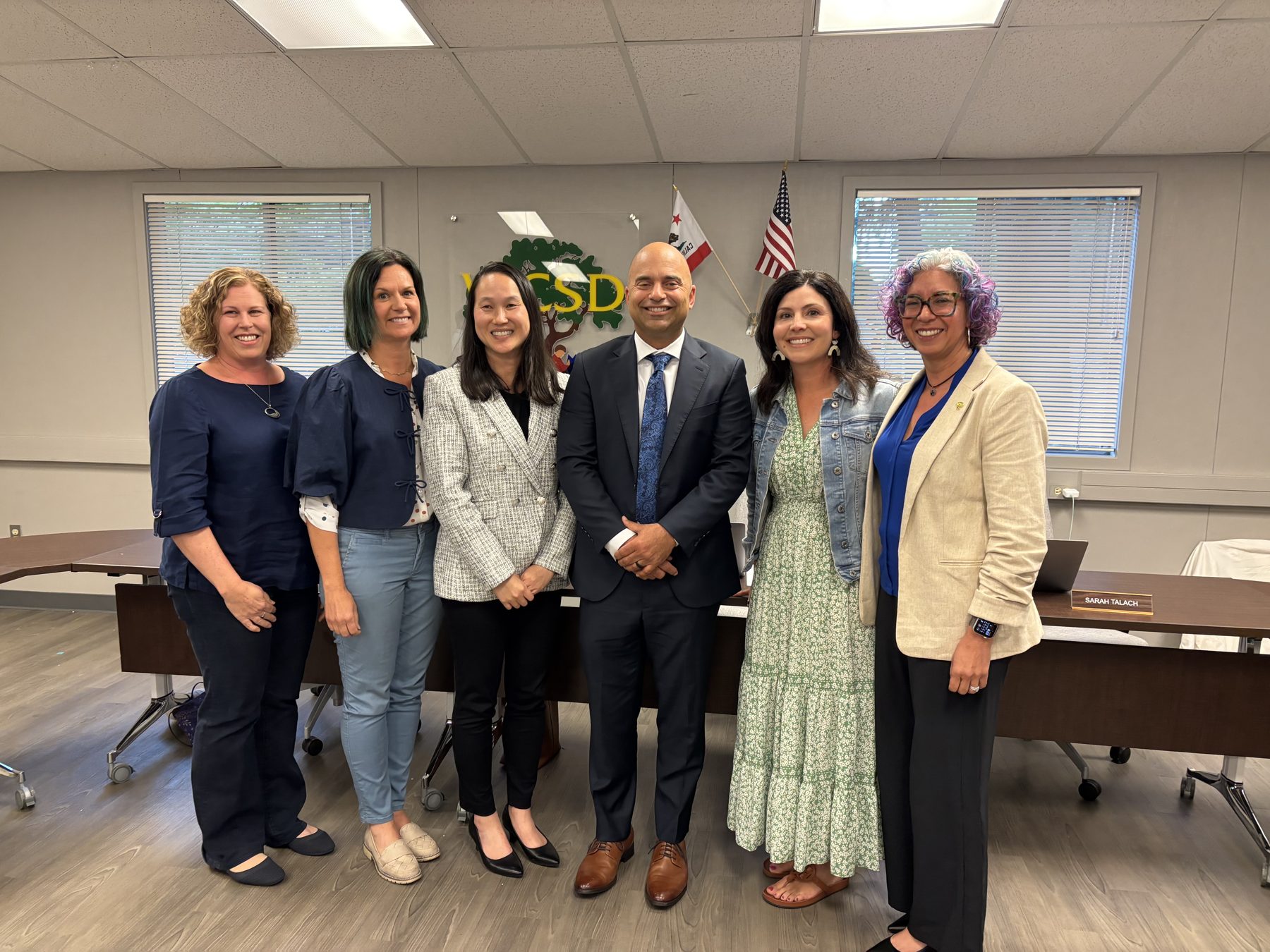 Six people standing together in the Walnut Creek School District boardroom. Wenlei Johnson is third from the left.